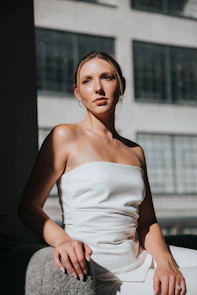 Model sitting on a white chair wearing beige flats, sunlight highlighting textures.