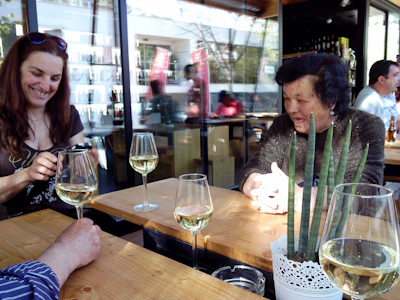 Casual daytime scene of a restaurant terrace bathed in natural light with customers enjoying wine and conversation.