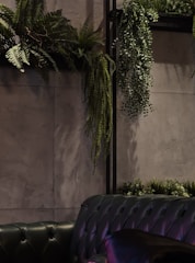 Lush hanging artificial ferns cascading gracefully from a modern black metal plant stand in a cozy living room corner.