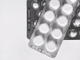 Two blister packs showing circular tablets with a line across the center, placed on a plain surface. The image is in black and white, emphasizing the texture and form of the packaging.