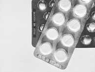 Two blister packs showing circular tablets with a line across the center, placed on a plain surface. The image is in black and white, emphasizing the texture and form of the packaging.