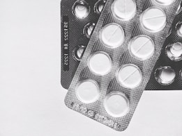Two blister packs showing circular tablets with a line across the center, placed on a plain surface. The image is in black and white, emphasizing the texture and form of the packaging.