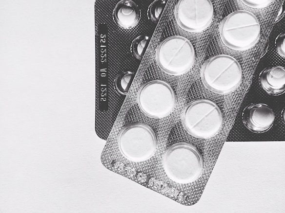 Two blister packs showing circular tablets with a line across the center, placed on a plain surface. The image is in black and white, emphasizing the texture and form of the packaging.