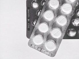 Two blister packs showing circular tablets with a line across the center, placed on a plain surface. The image is in black and white, emphasizing the texture and form of the packaging.