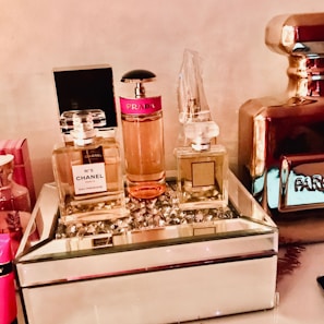 A collection of various perfume bottles arranged on a mirrored tray with decorative crystal embellishments. The bottles are of different sizes and designs, including recognizable brands with elegant labeling. The setting exudes a luxurious and sophisticated ambiance.