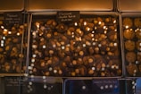 A glass display case presents an assortment of chocolate confections. The chocolates are topped with various nuts, including almonds and hazelnuts. Labels, written in French, are placed above each section, indicating the type of chocolate and toppings. The warm lighting reflects off the glass, adding a cozy and inviting atmosphere.