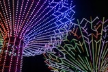 A vibrant display of multicolored LED lights arranged in radiating patterns forming intricate designs against a black background. The lights transition through a spectrum of colors including red, blue, green, and purple, creating a mesmerizing visual effect.