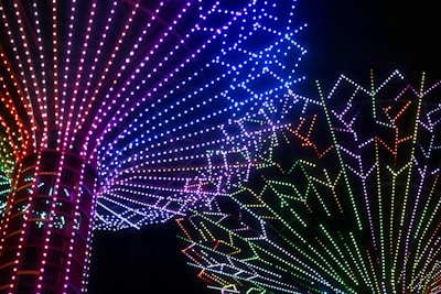 A vibrant display of multicolored LED lights arranged in radiating patterns forming intricate designs against a black background. The lights transition through a spectrum of colors including red, blue, green, and purple, creating a mesmerizing visual effect.