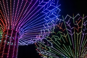A vibrant display of multicolored LED lights arranged in radiating patterns forming intricate designs against a black background. The lights transition through a spectrum of colors including red, blue, green, and purple, creating a mesmerizing visual effect.