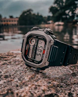 Sporty digital watch with a rugged black band resting on a rock outdoors.