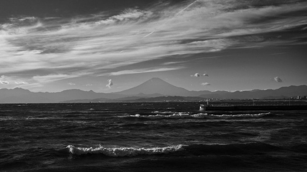 a black and white photo of the ocean with mountains in the background