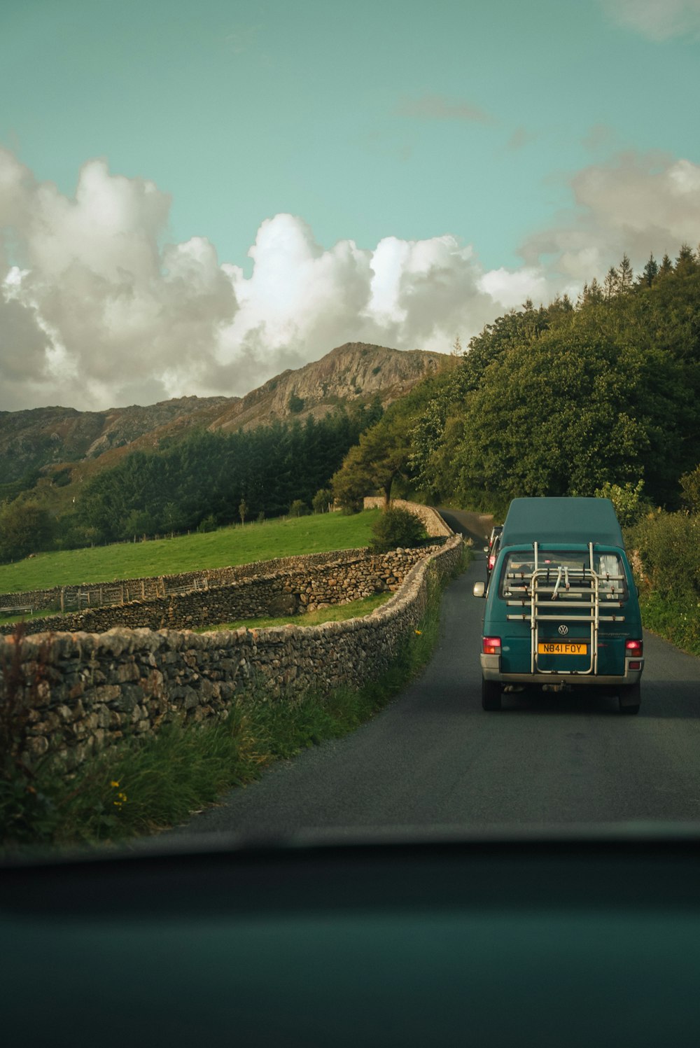 a van driving down a road next to a lush green hillside