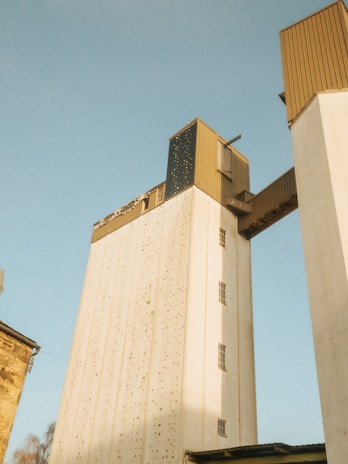 Tall industrial buildings with a high connecting bridge, featuring structures with brown and white exteriors under a clear, pale blue sky.