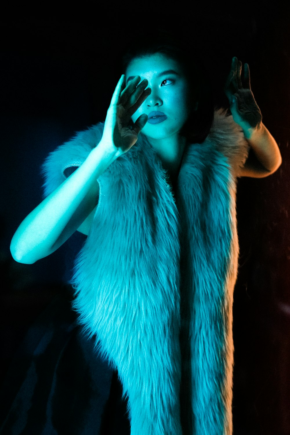 a woman in a fur vest holding her hand up to her face