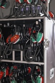 A collection of green and red headsets with attached microphones organized inside a storage case. The headsets are connected with coiled cables to communication devices stored in the same compartment. The equipment appears neatly arranged, suggesting a professional setting, likely related to aviation or motorsports.