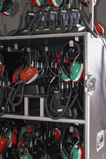 A collection of green and red headsets with attached microphones organized inside a storage case. The headsets are connected with coiled cables to communication devices stored in the same compartment. The equipment appears neatly arranged, suggesting a professional setting, likely related to aviation or motorsports.