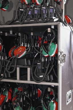 A collection of green and red headsets with attached microphones organized inside a storage case. The headsets are connected with coiled cables to communication devices stored in the same compartment. The equipment appears neatly arranged, suggesting a professional setting, likely related to aviation or motorsports.