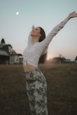 A woman standing in a field at sunrise, arms raised in joyful worship.