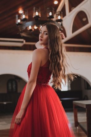 A vibrant red cocktail dress hanging against a soft cream background.