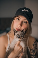 a woman holding a cat while wearing a hat