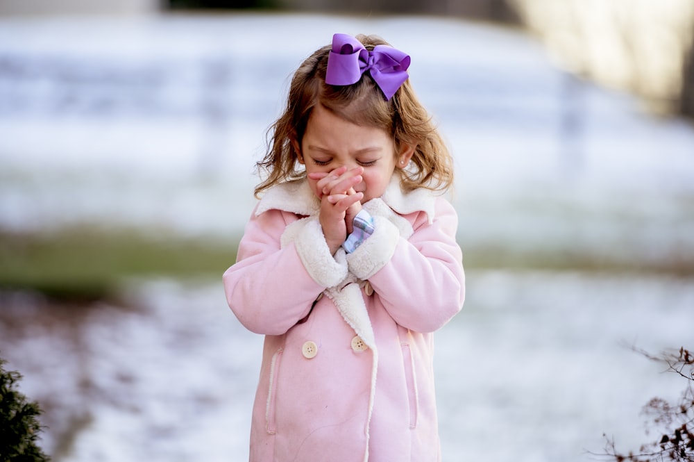 a little girl in a pink coat holding her hands together