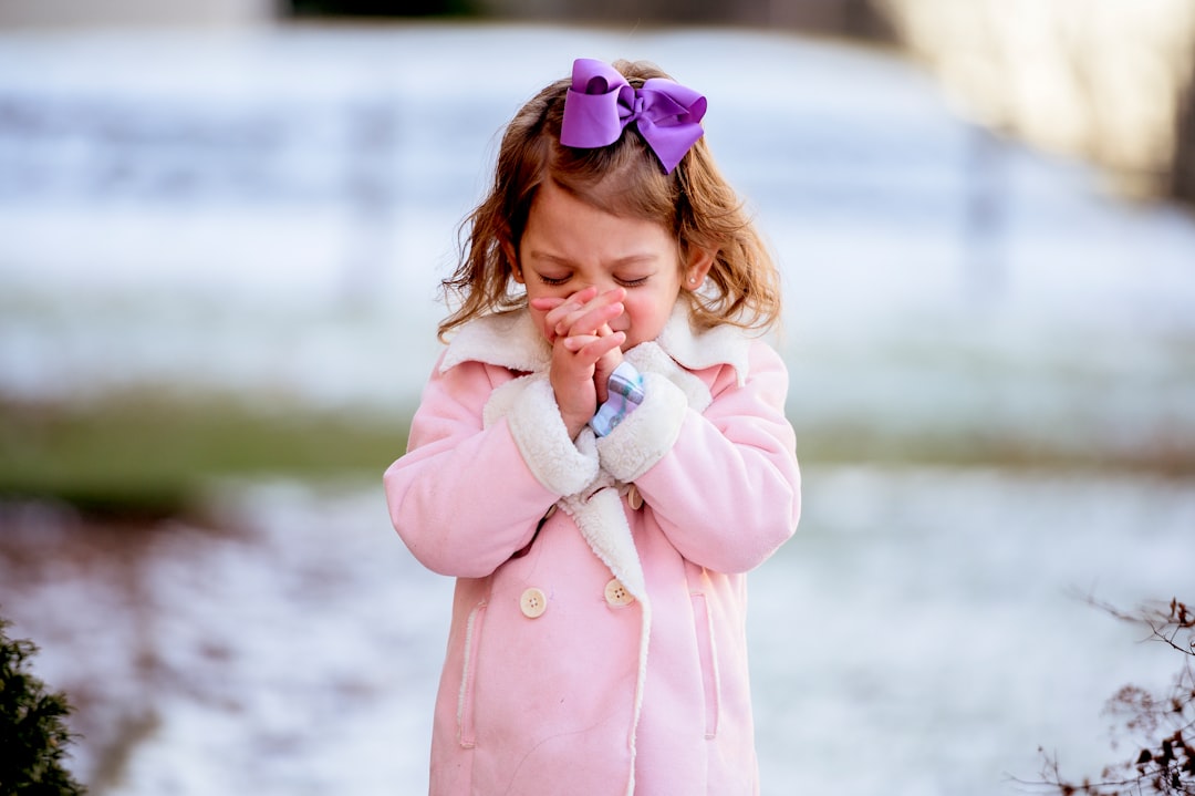 a little girl in a pink coat holding her hands together