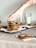 A hand with a tattoo reaches for a stack of homemade cookies on a cooling rack. The cookies are topped with white and dark chocolate chunks along with dried red fruit. A glass of milk sits in the background on a beige tablecloth, contributing to a cozy, homey atmosphere.