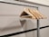 A series of wooden coat hangers are neatly aligned on a metal clothing rack, against a plain wall with a shadow cast by the hangers. The hangers are angled in different directions, creating a visually interesting pattern.