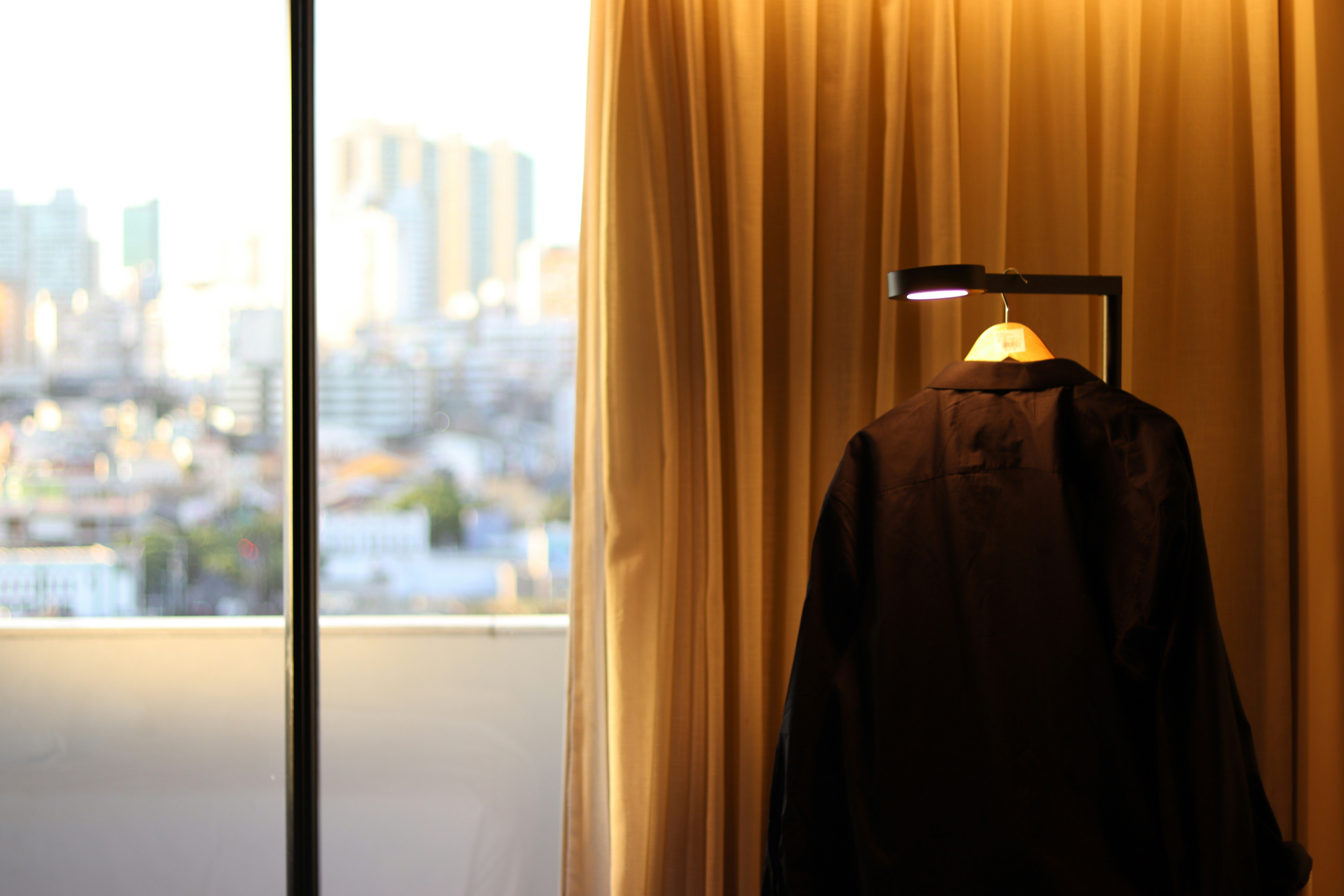 Black jacket hangs on a hanger before golden curtains.