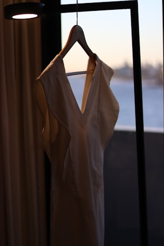 Close-up of a flowy beach dress hanging on a wooden rack with sunlight filtering through.