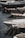 Several luxury yachts are docked in a marina, with their sleek designs and polished surfaces. The yachts are lined up closely, each tied with ropes to the dock. The water reflects the hulls of the boats, creating a calm and serene atmosphere.