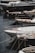 Several luxury yachts are docked in a marina, with their sleek designs and polished surfaces. The yachts are lined up closely, each tied with ropes to the dock. The water reflects the hulls of the boats, creating a calm and serene atmosphere.