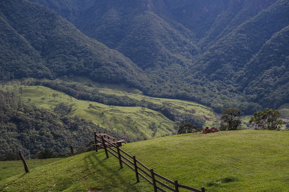 a wooden fence on a grassy hill with mountains in the background