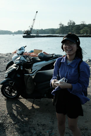 A local driver partner smiling next to his scooter on a sunny Bali street.