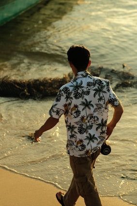 A sunlit beach scene with a model wearing a breezy linen shirt, walking along the shoreline.