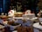 A selection of desserts and pastries displayed on a table, with a festive Christmas theme. Various cakes, cookies, and sweets are arranged on white plates and stands, some adorned with decorations such as strawberries. There are labels for each dessert including 'Coffee Butter Bar', 'Sweet Pumpkin Crumble', and 'Victoria'. The background features a decorated Christmas tree with lights and ornaments, adding a holiday ambiance.