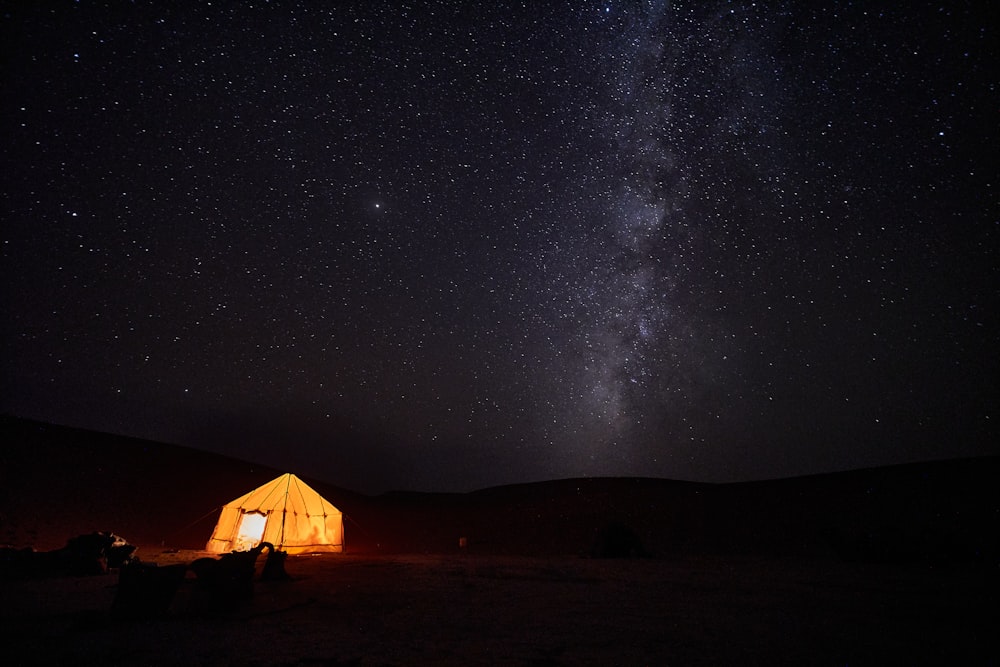 a tent in the middle of a field under a night sky filled with stars