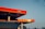 A modern gas station with a prominently displayed red sign reading 'CNG'. The structure features a clean, angular design with bright red and orange tones. The sky is clear with a gradient from light blue to pale orange near the horizon.