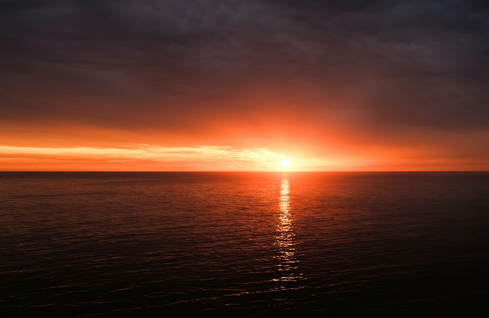 the sun is setting over the ocean on a cloudy day