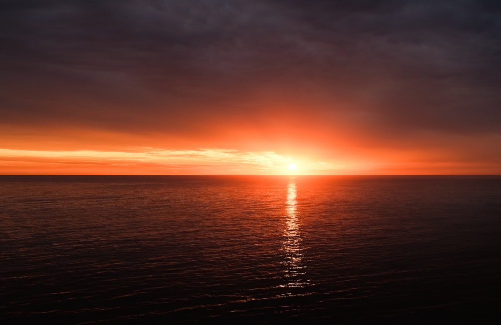 the sun is setting over the ocean on a cloudy day