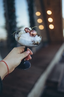 A lifestyle shot of a hand holding a snow globe flask against a backdrop of soft pink roses and warm lighting.