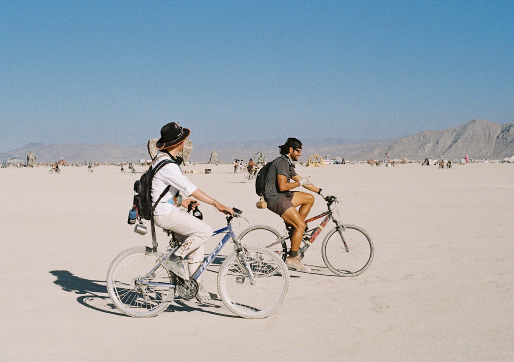 a couple of people riding bikes across a sandy field
