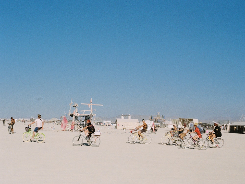 a group of people riding bikes on top of a sandy beach