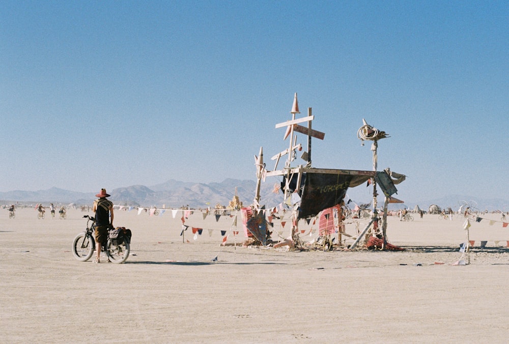 a man riding a bike next to a cross on a beach