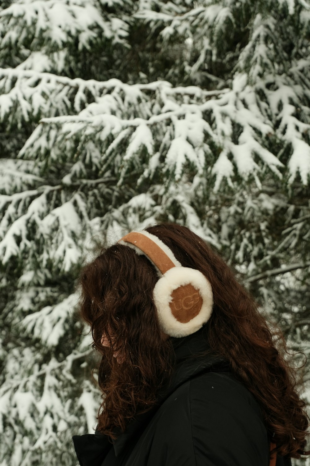 a woman wearing ear muffs standing in front of snow covered trees