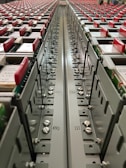 A close-up view down the center of a series of industrial electrical or communication panels, featuring rows of red tabs on each panel. Labeling and numbers are present on the metal surface, indicating organization and connectivity with screws and bolts as part of the assembly.