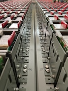 A close-up view down the center of a series of industrial electrical or communication panels, featuring rows of red tabs on each panel. Labeling and numbers are present on the metal surface, indicating organization and connectivity with screws and bolts as part of the assembly.