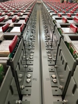 A close-up view down the center of a series of industrial electrical or communication panels, featuring rows of red tabs on each panel. Labeling and numbers are present on the metal surface, indicating organization and connectivity with screws and bolts as part of the assembly.