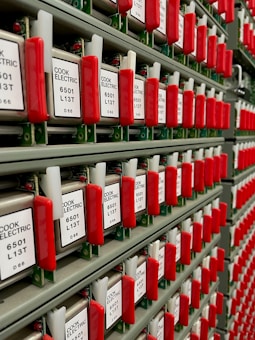 Rows of vintage electrical components with red handles and labels reading 'Cook Electric'. Each component has a label with letters and numbers.