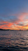 A vibrant sunset over a calm sea with a ferry sailing in the distance.
